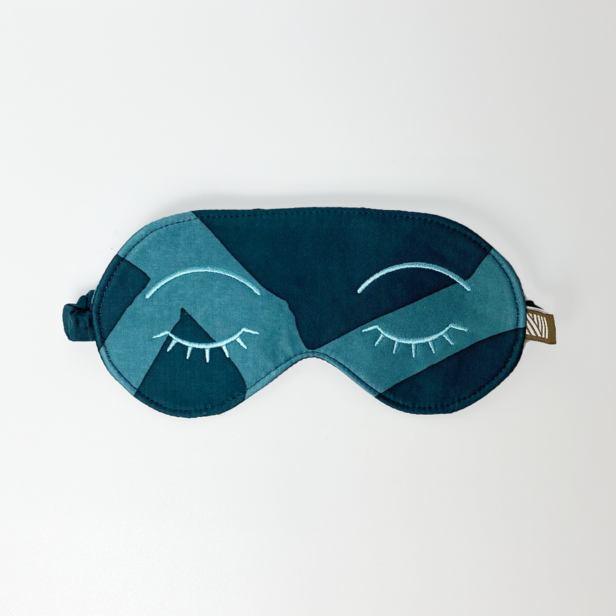 an eye mask made of batik in the pattern forest green in front of a neutral background