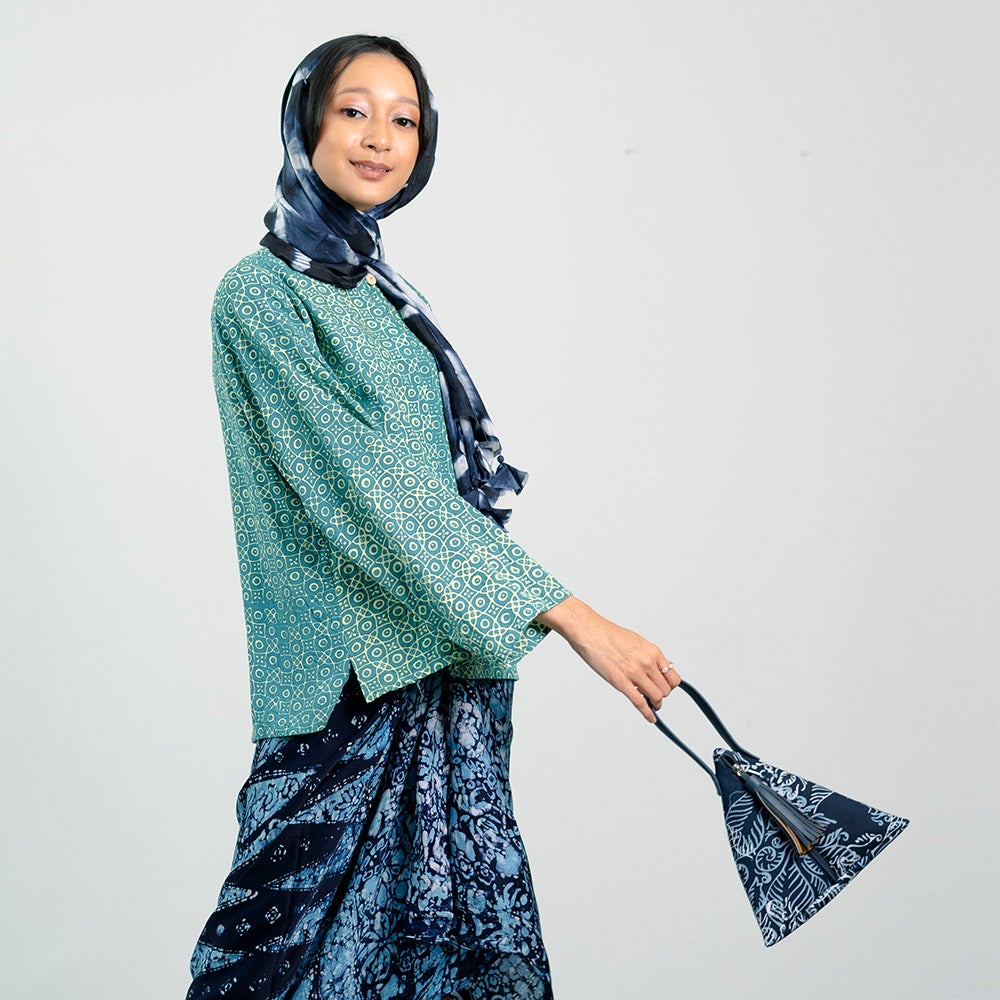 a model in traditional clothing holding a bag made of batik in the pattern blue nautical fern in front of a neutral background