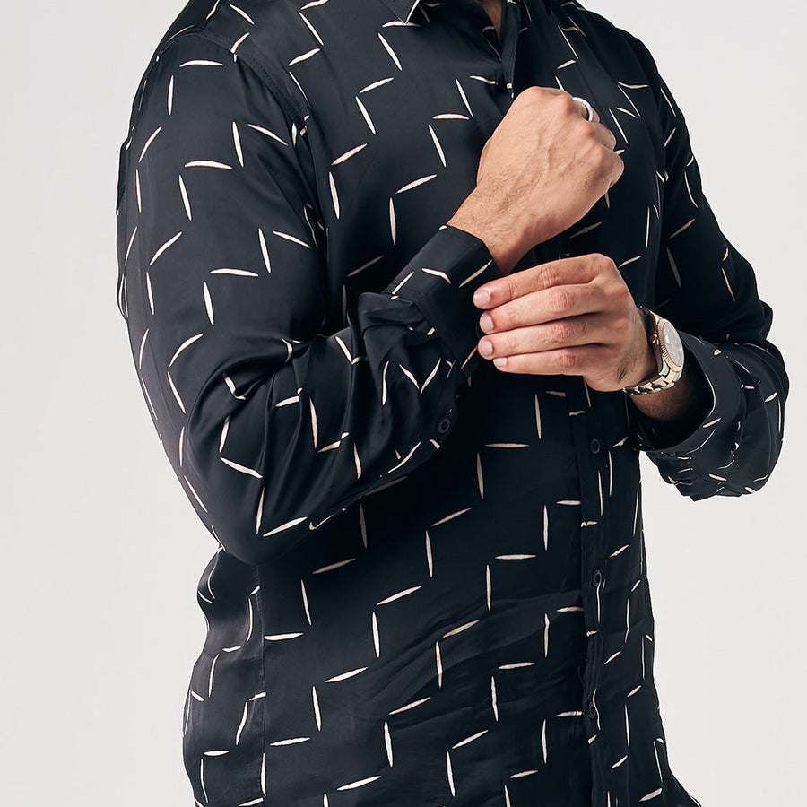 A closeup photo showing a man is wearing batik long sleeve shirt in Jet Tangga, black color shirt. While posing in front of white background. He is showing the button on the sleeve of the shirt