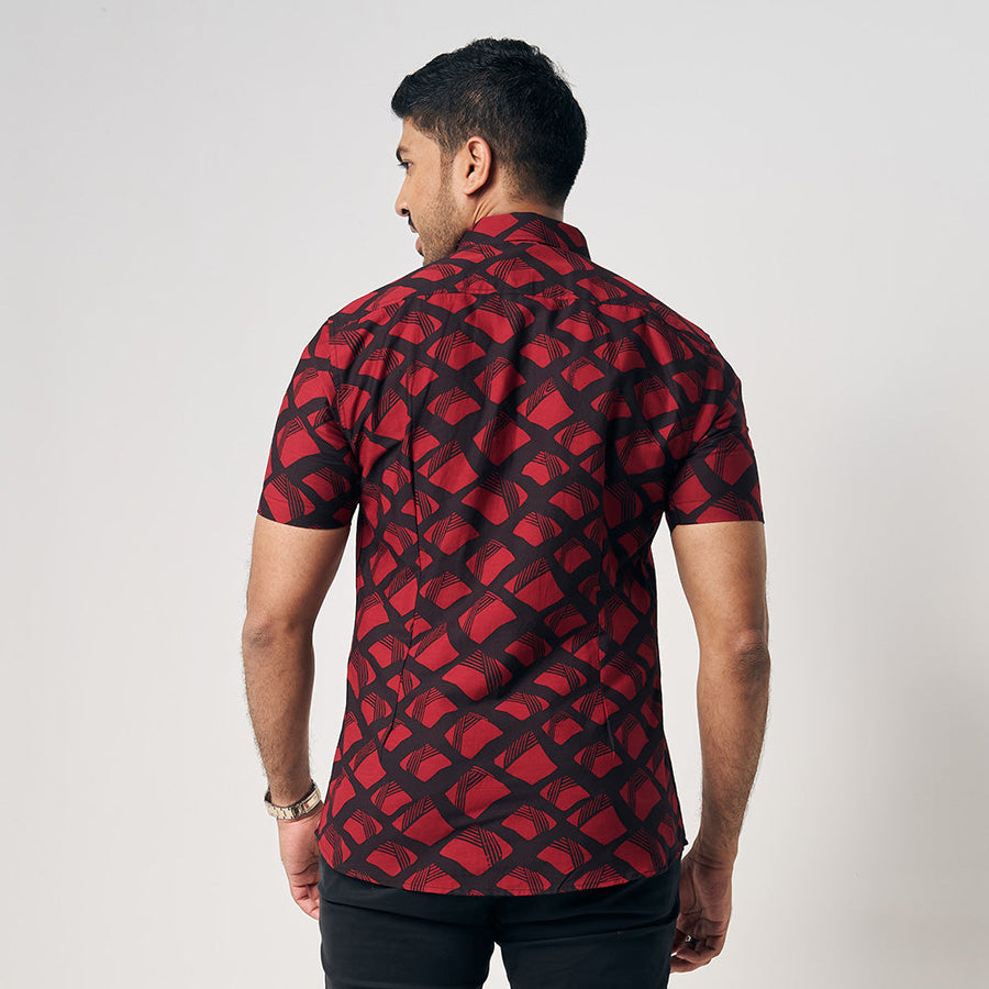 A man is wearing handcrafted batik short sleeve shirt in Red Nasi Lemak, black and red color shirt. While posing in front of white background