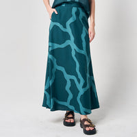 A woman gracefully adorned in a long batik skirt featuring the Forest Chain pattern, showcased against a neutral background, capturing the elegance of the design