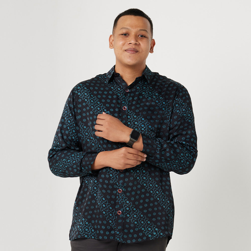 a man posing in front of a white wall wearing a watch and a batik shirt in black alur