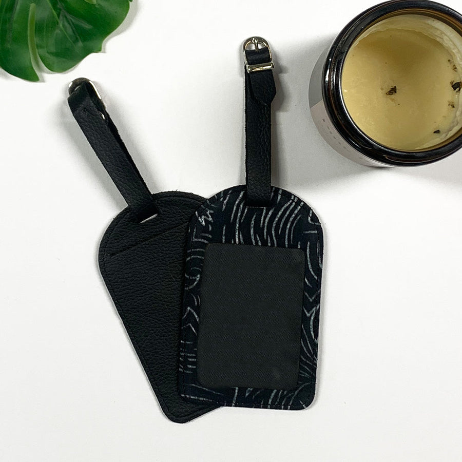 a lifestyle photo of luggage tag made of batik remnants in black driftwood against a neutral background with a candle and a tropical leaf decorations