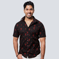 a man posing in front of a white wall while wearing a batik shirt in black palm pattern