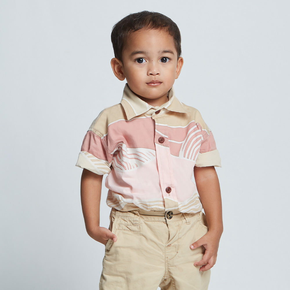 Young boy wearing pink batik shirt with wooden buttons and tan trousers.