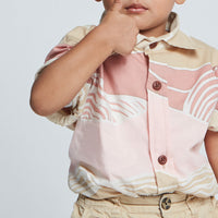 Close up of young boy wearing pink and tan batik shirt with wooden button at front from Raya 2023 collection. 