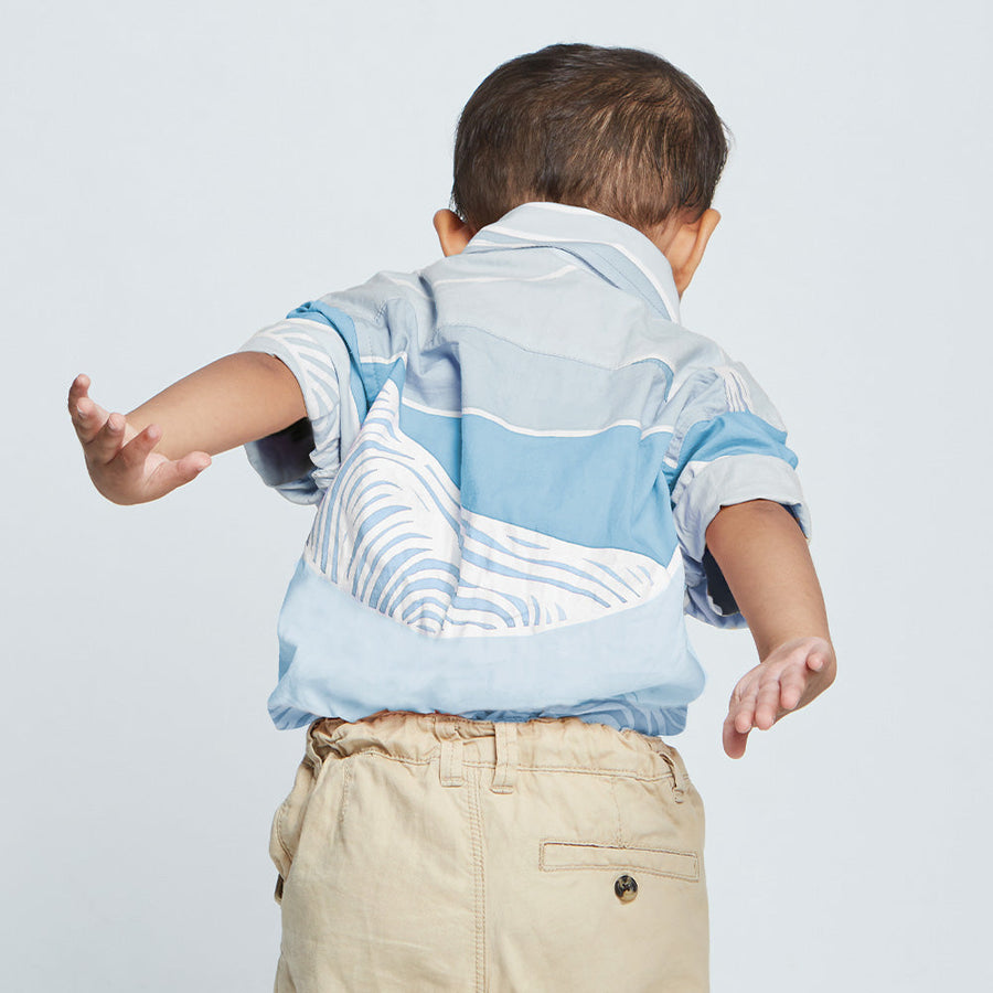 Back view of boy in blue batik shirt with his arms playfulling pretenting to fly.