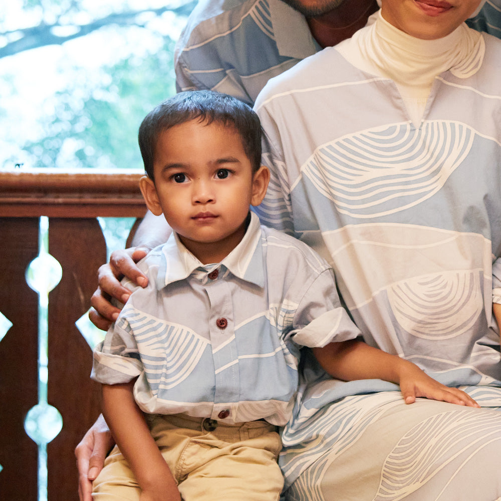 Close-up of mother and son in matching blue batik apparel. Boy in blue batik shirt and mother in blue batik baju kedah sitting on a bench.