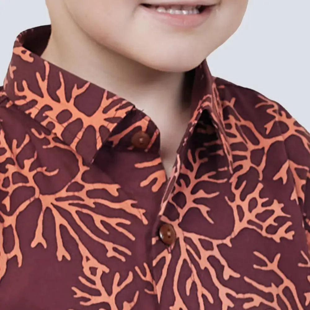 A captivating close-up shot featuring a young boy wearing an authentic Maroon Coral patterned batik shirt against a neutral background