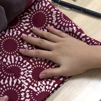 a photo of a seamstress in the process of sewing a batik in the pattern crimson lunar