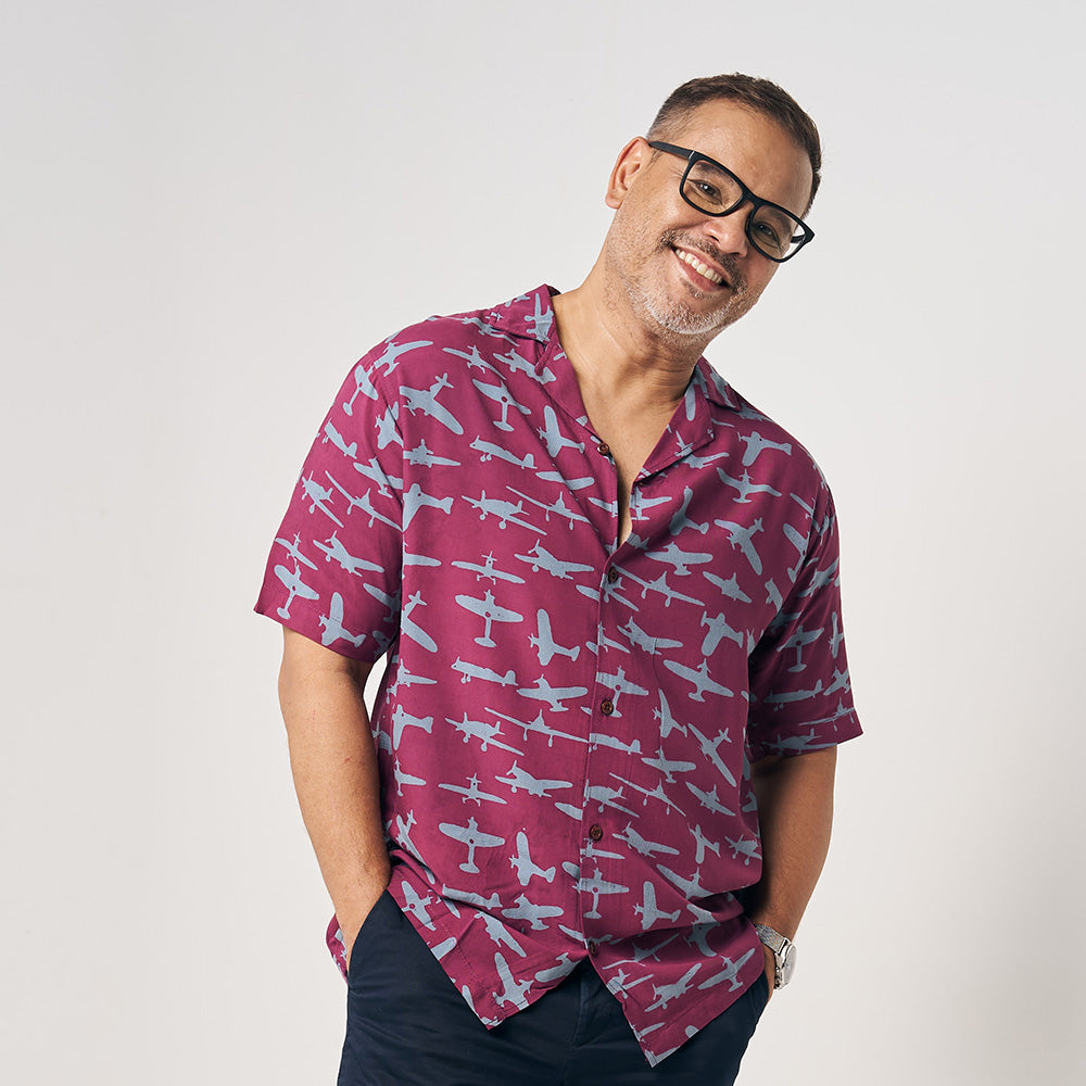 a man in front of a neutral background showcasing a batik shirt in the pattern garnet airplane