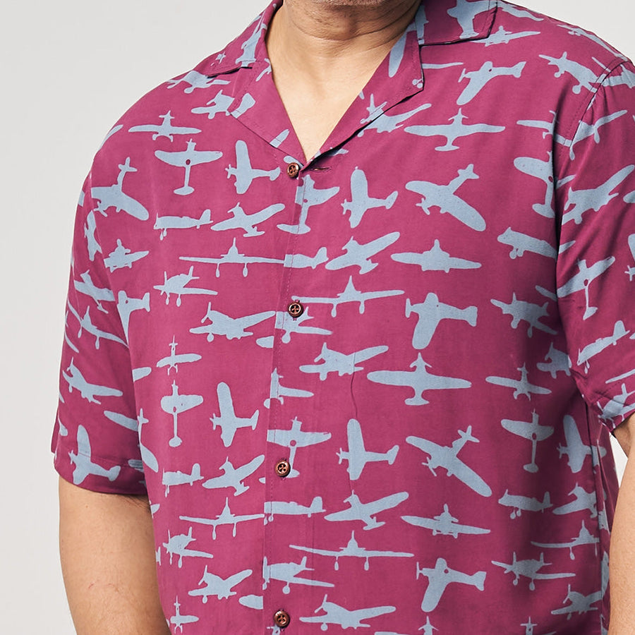 a man in front of a neutral background showcasing a batik shirt in the pattern garnet airplane