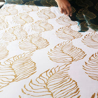 An artisan is painting on a white fabric that has been waxed with fern pattern