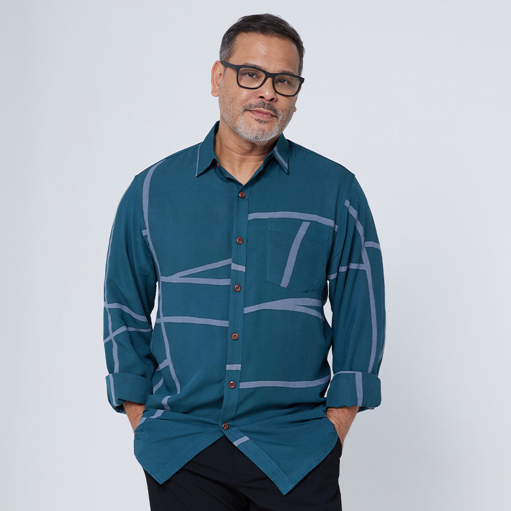 A man standing in front of a white wall while wearing a long-sleeved batik shirt in Forest Green