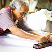 An artisans is using technique of blocking batik on white fabric