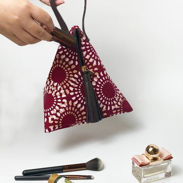 a lifestyle photo of handcrafted batik ketupat bag in crimson lunar showing a woman hand holding the bag while insert lipstick in the bag