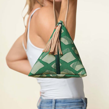 a model showcasing a bag made of batik in the shape similar to a ketupat, in the pattern green nasi lemak in front of a neutral background
