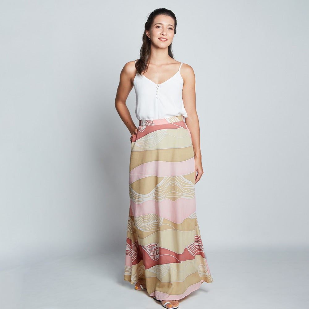 Full view of female model wearing long flair pink batik skirt and white camisole.