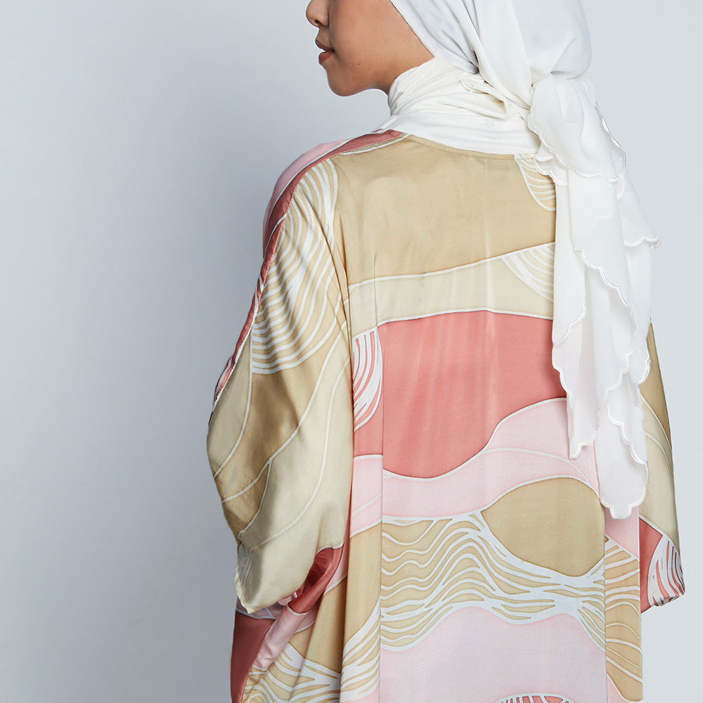 Close-up of back of woman in long batik kimono, hand-drawn Dawn Bukit print in pink, tan, and white.