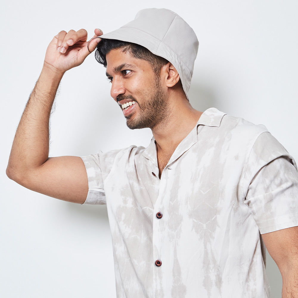 a man posing in front of a white wall while wearing a shibori cuban shirt in mangosteen