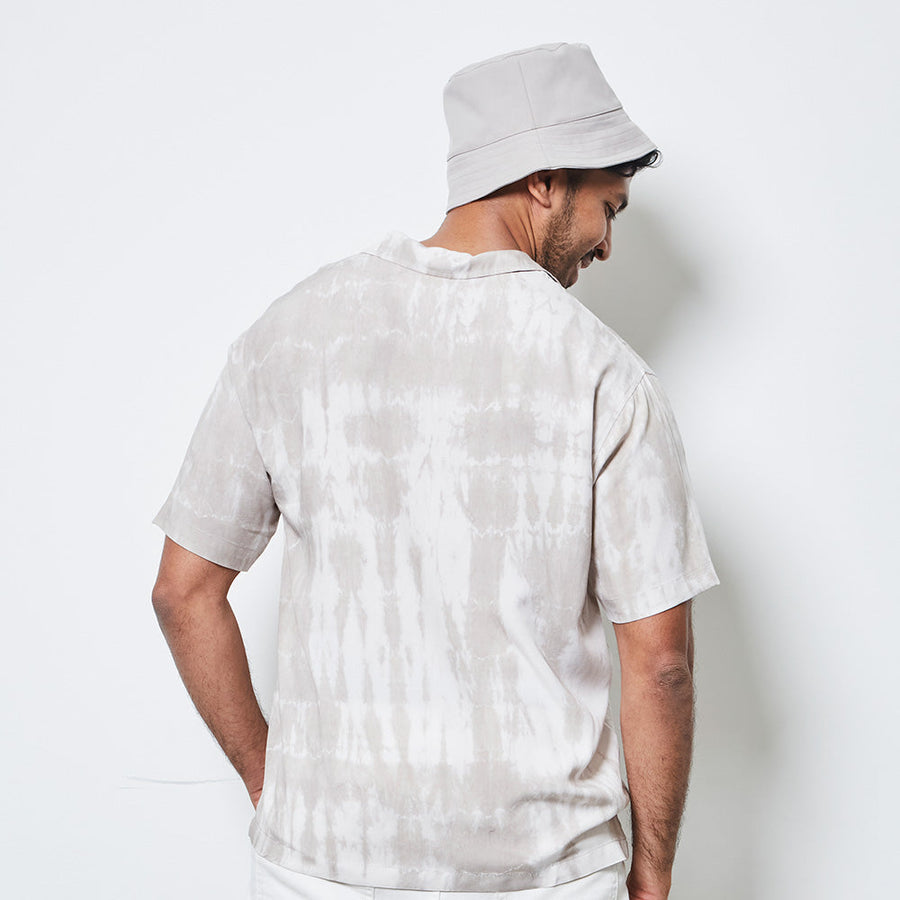 a man facing a white wall while wearing a shibori cuban shirt in mangosteen