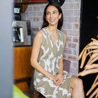 a lifestyle photo of woman wearing batik dress in stone chain pattern sitting on a chair with pantry as background