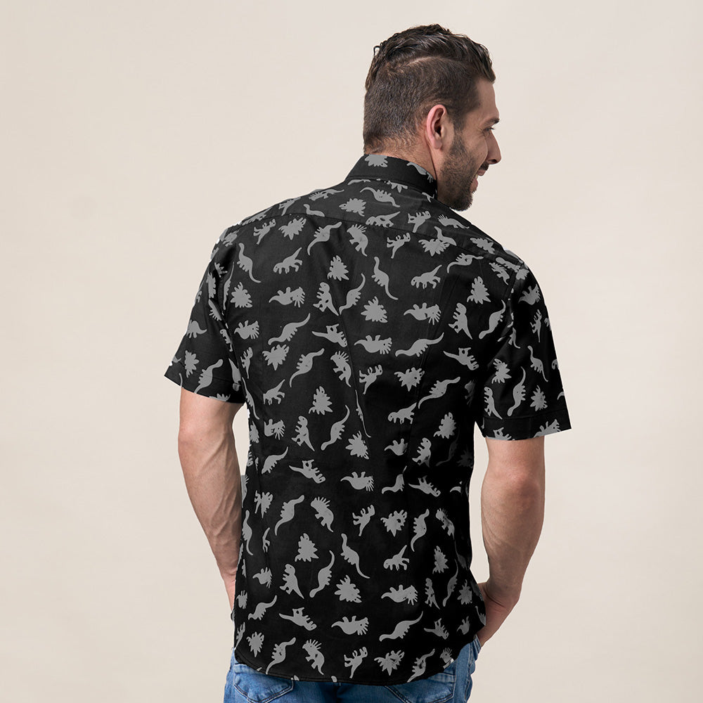 a photo of a man posing with his back to the camera in front of a wall while wearing a dinosaur batik shirt in the color grey