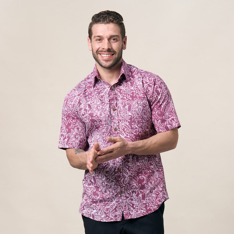 A male model posing in front of a neutral background while wearing a batik shirt made in the pattern pink floret