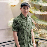 In a nature-infused lifestyle photo, a man exudes style while wearing an authentic Forest Arabesque patterned batik shirt, surrounded by lush greenery