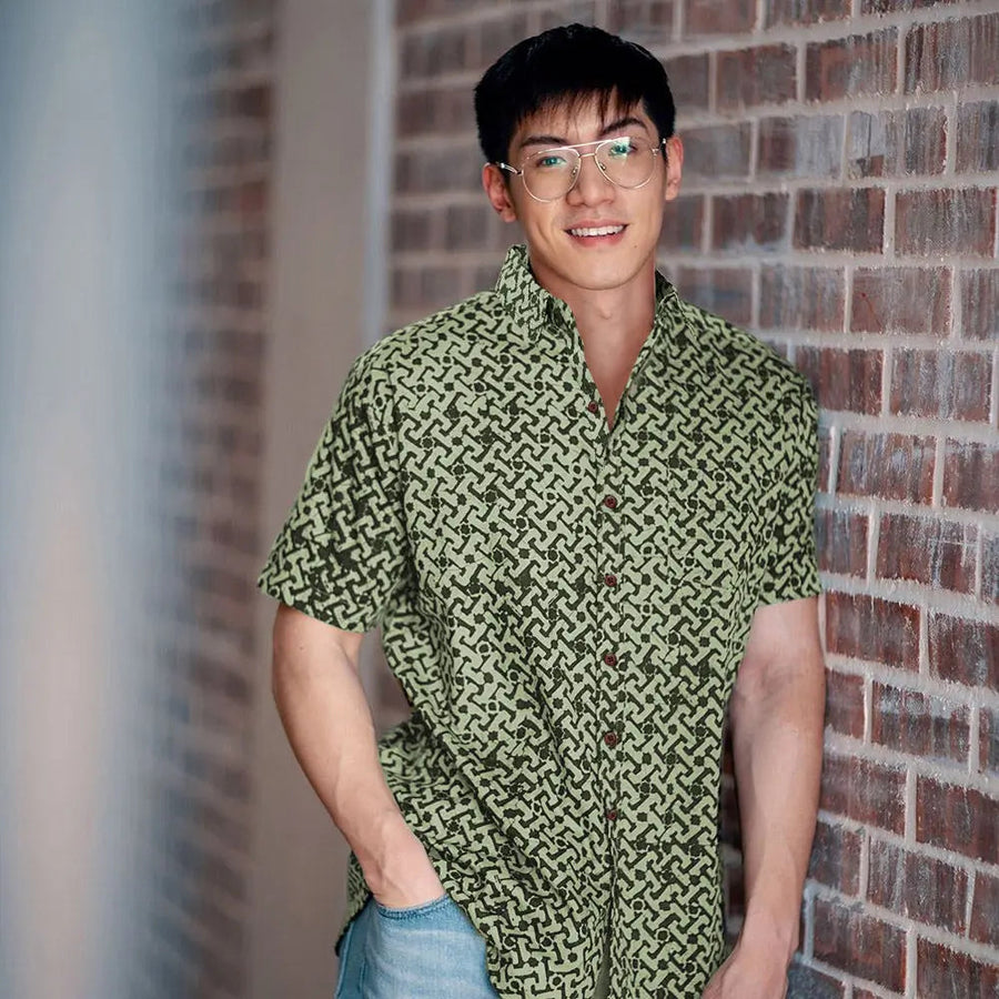 A captivating lifestyle image capturing a model's pose against a rustic brick wall, dressed in a striking batik shirt featuring the Forest Arabesque pattern