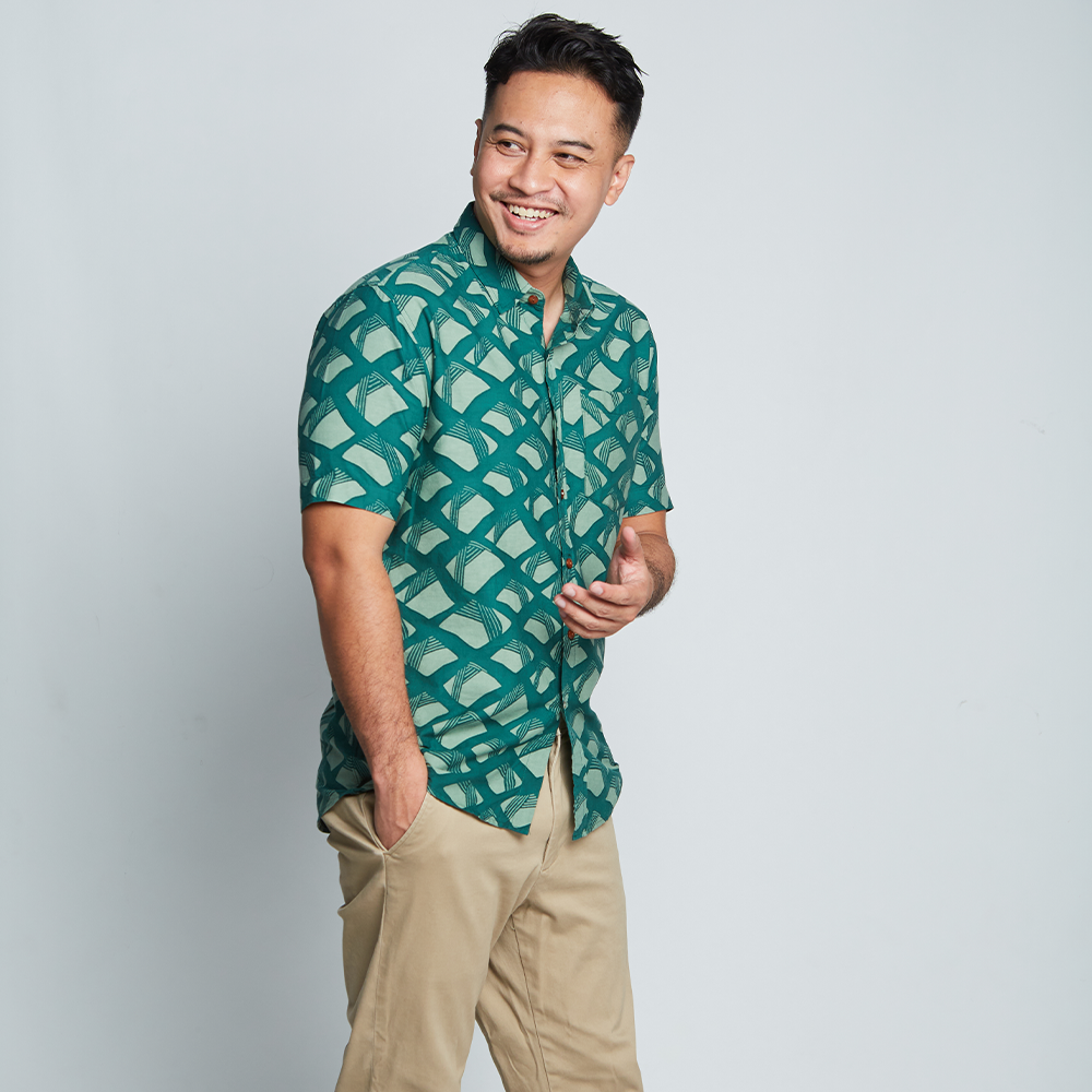 a man posing happily in front of a neutral background in an authentic batik shirt in the pattern green nasi lemak made by malaysian artisans