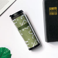 a batik tumbler in the pattern olive diwanie laying on a white surface surrounded by a black box with the batik boutique logo on the box, a leaf and a book
