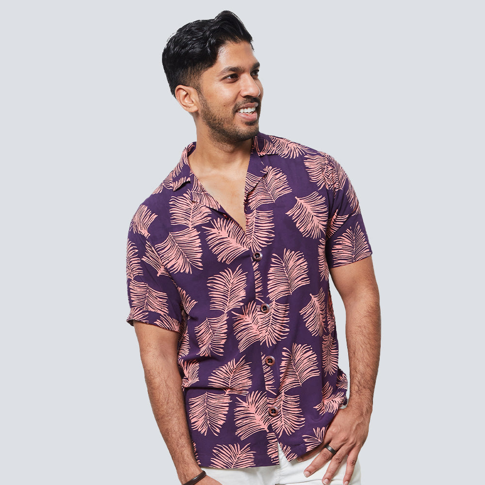 a man posing in front of a white wall while wearing a batik shirt in purple sawit pattern