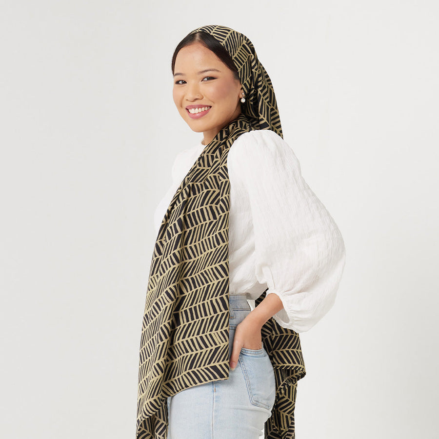  a woman standing in front white background styling batik scarf in black banana leaf pattern