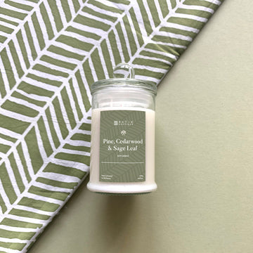 a pine, cedarwood and sage leaf candle sits in front of a wall with a similar patterned batik