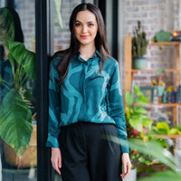 In a picturesque lifestyle photo, a woman exudes elegance while posing in a green batik shirt adorned with the Forest Chain pattern, surrounded by lush greenery