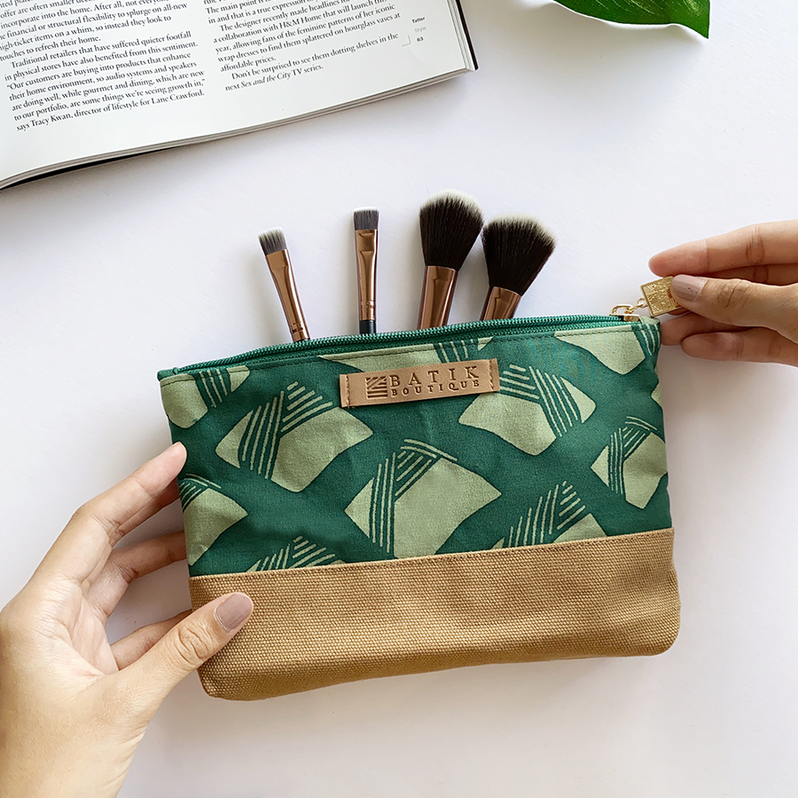 a lifestyle photo of a zip pouch made of batik in the color green nasi lemak against a neutral background