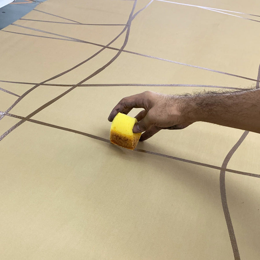 an artisan is drawing wax line on a beige color fabric